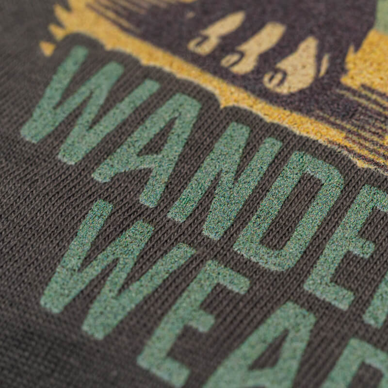 Close-up of Wilderness Watcher graphic tee showing textured Wanderlust Wear Co. logo and vintage ink detailing on fabric