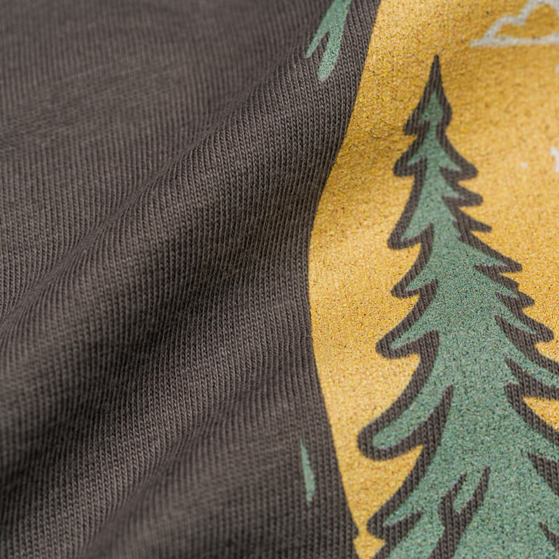 Close-up of Wilderness Watcher graphic tee print showing pine tree detail and vintage ink texture on soft cotton fabric