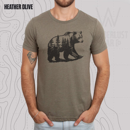 Model wearing Roam Wild Bear graphic tee in Heather Olive, featuring hand-drawn bear silhouette with pine trees and Wanderlust Wear Co. branding