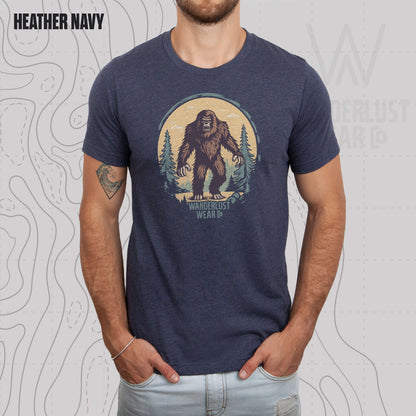 Model wearing Wilderness Watcher graphic tee in Heather Navy, featuring hand-drawn bear silhouette with pine trees and Wanderlust Wear Co. branding