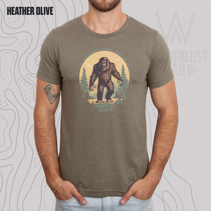 Model wearing Wilderness Watcher graphic tee in Heather Olive, featuring hand-drawn bear silhouette with pine trees and Wanderlust Wear Co. branding