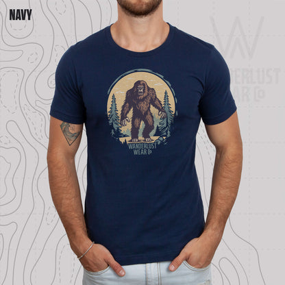 Model wearing Wilderness Watcher graphic tee in Navy, featuring hand-drawn bear silhouette with pine trees and Wanderlust Wear Co. branding